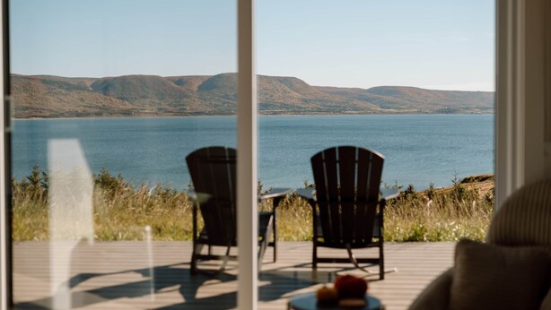 Vista desde una habitación con dos sillas que dan a un lago, con colinas al fondo.