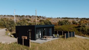 Un edificio moderno de color negro con un patio, rodeado de paisaje natural y líneas eléctricas.