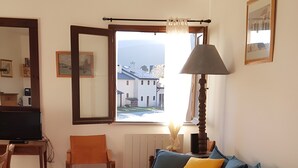A living room with a teal sofa, a wooden chair, a lamp, and a window with a view of buildings.
