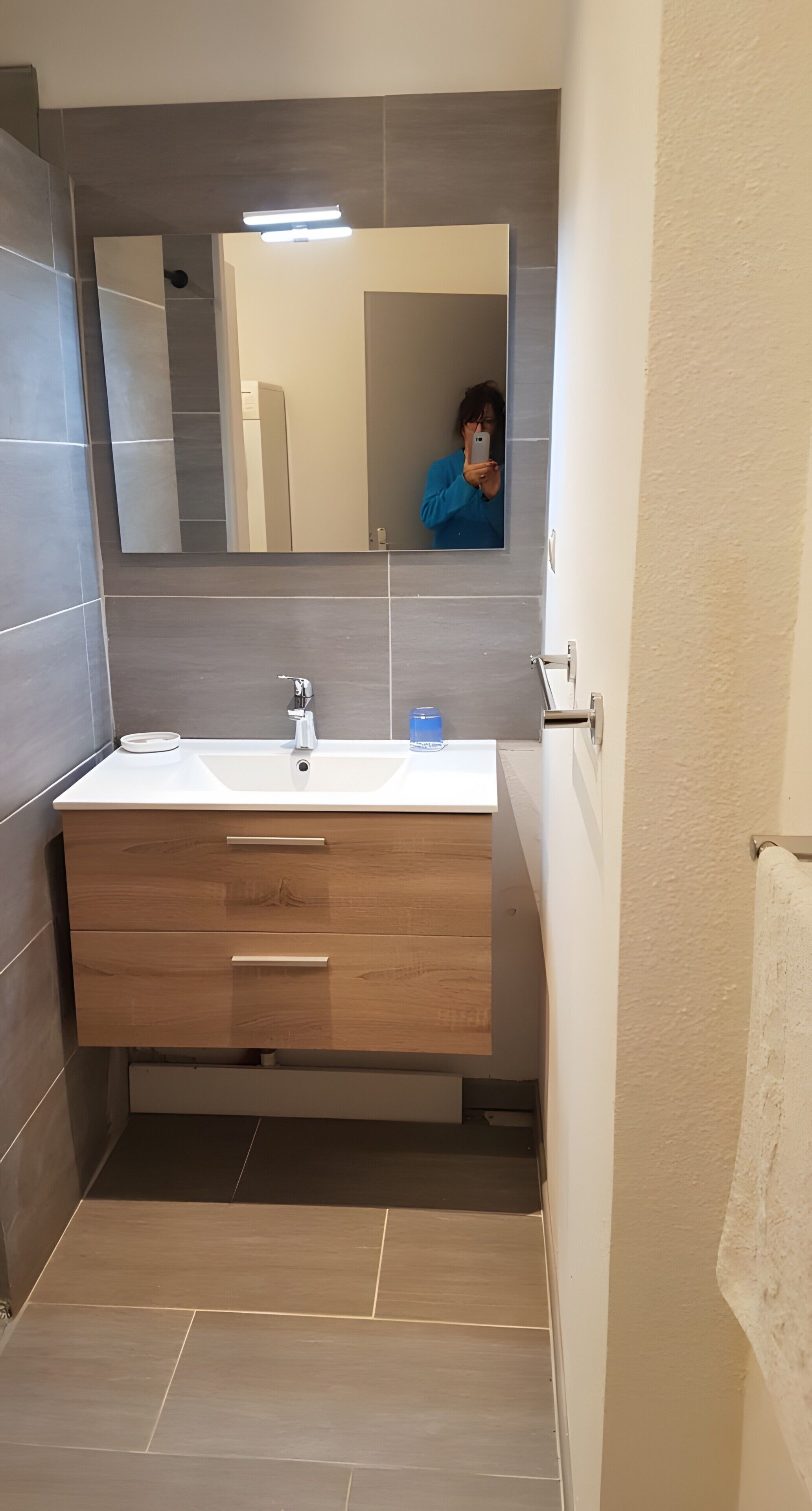 Een moderne badkamer met een witte wasbak, een houten wastafelmeubel en een grote spiegel.