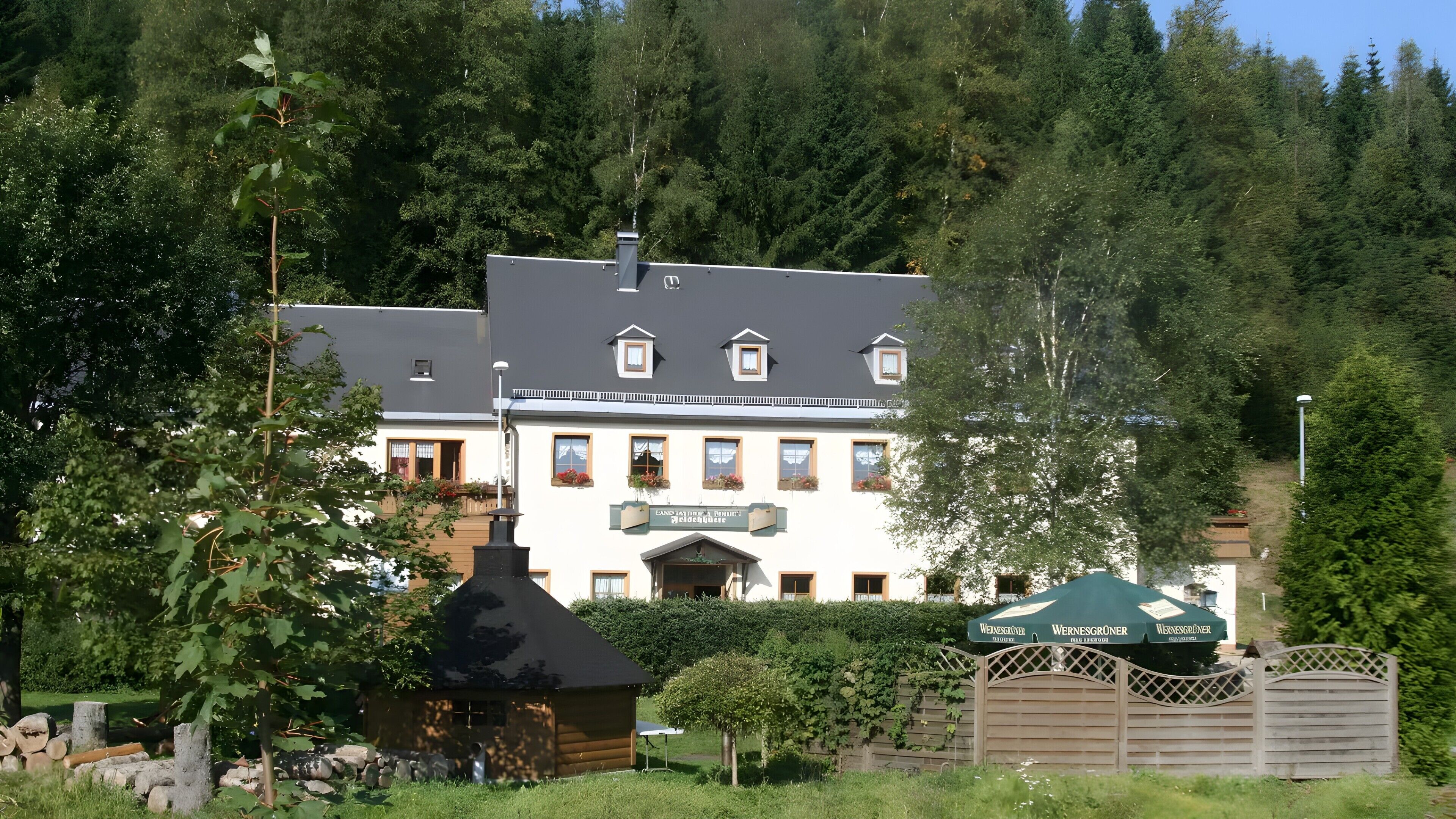 Un bâtiment sur lequel on peut lire l’inscription « Wernersgruner », entouré d’arbres et délimité par une clôture en bois.