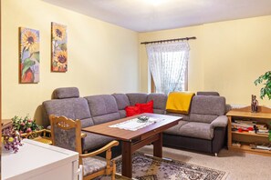 A living room with a sofa, a wooden table, a chair, a bookshelf, and two paintings on the wall.