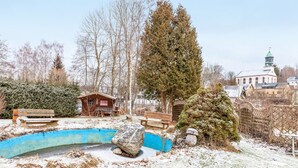 Un espace extérieur enneigé avec une petite structure en bois, un grand arbre et, au fond, un bâtiment doté d’un toit végétalisé.