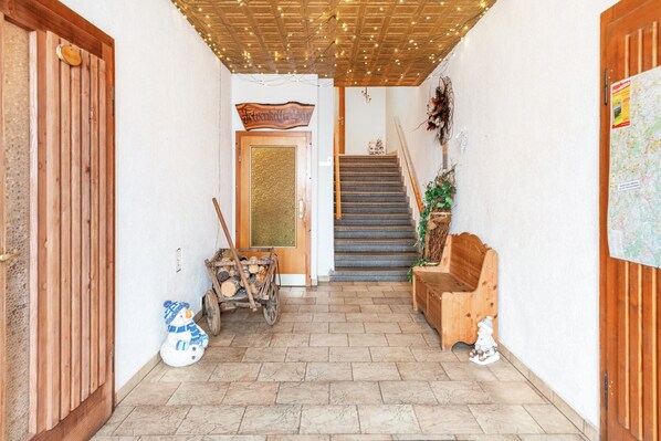 A hallway with a wooden door, a bench, a wooden cart with logs, and a staircase.