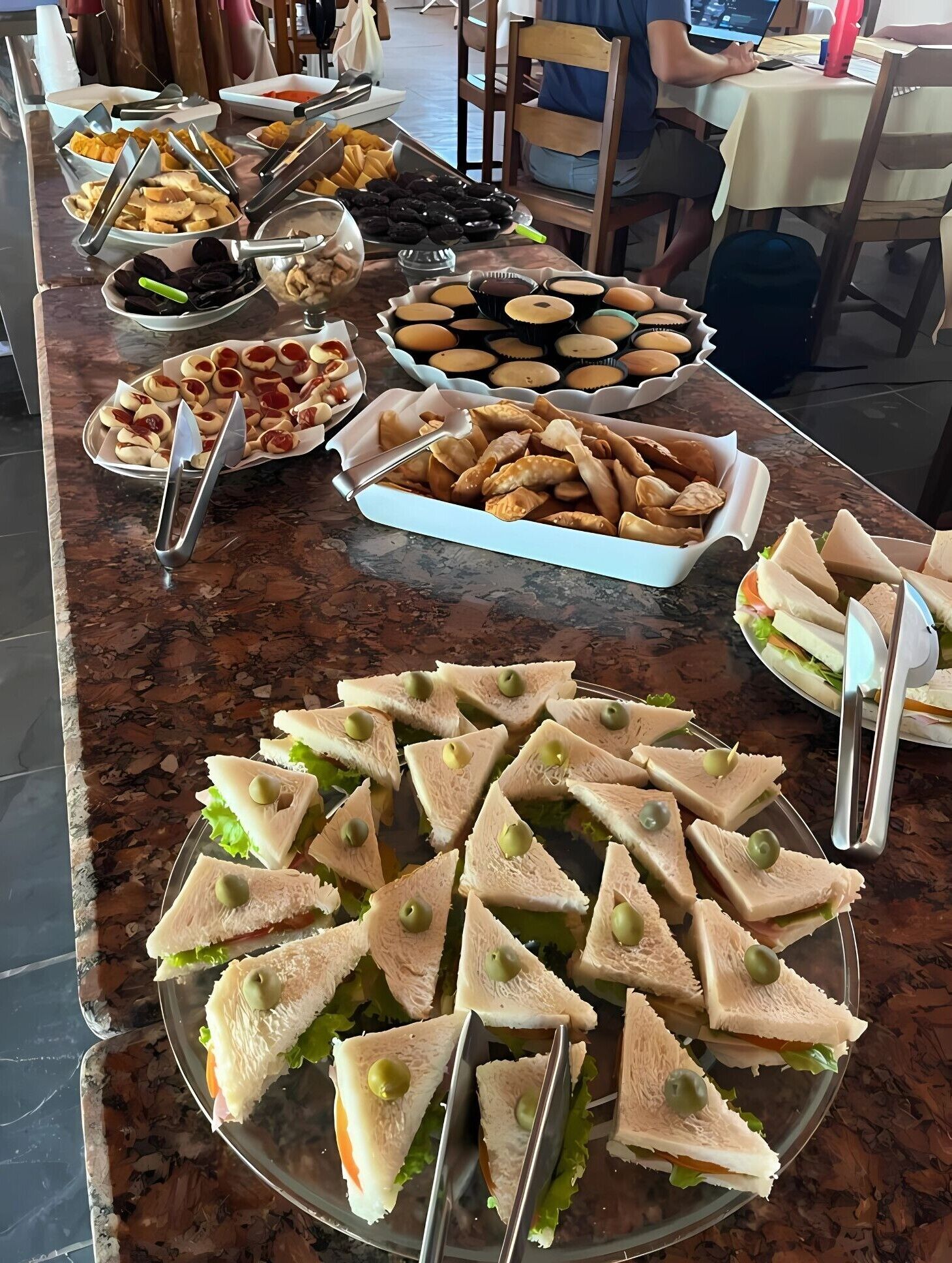 A buffet table with various food items including sandwiches, pastries, and other snacks.