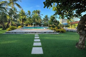 A well-maintained pool area with a clear pathway leading to the pool, surrounded by lush greenery and palm trees.