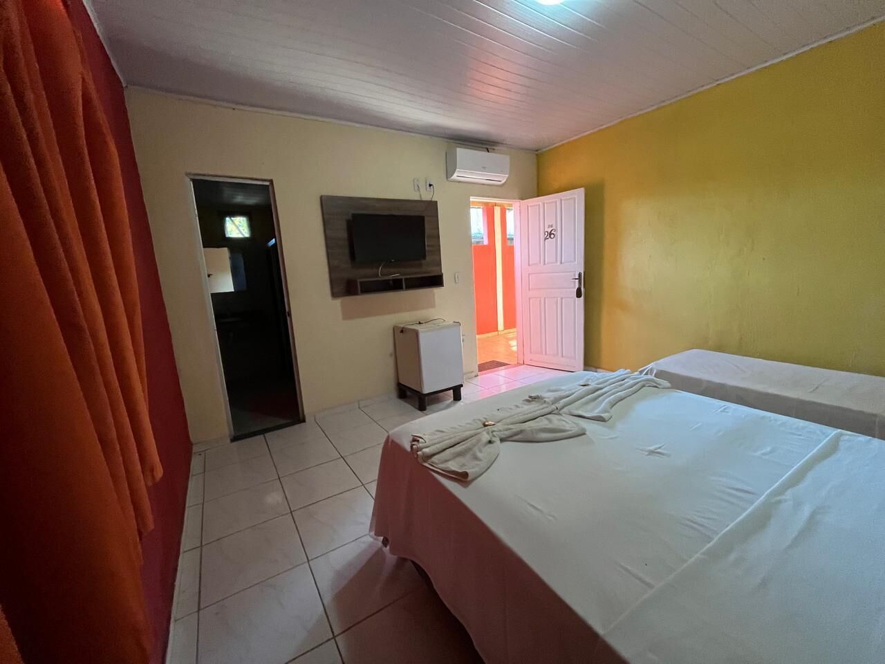 A hotel room with a bed, a television, a small cabinet, and a door leading to another room.