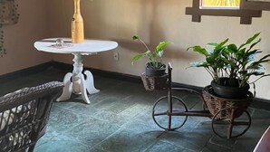A room with a round table, wicker chair, potted plants, and a decorative wall piece. - Pousada Taba de Canes (Canavieiras)