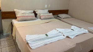 A hotel room with two beds, each with a beige bedspread and striped pillows. There are towels and a smartphone on the beds. - Pousada Taba de Canes (Canavieiras)