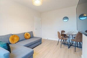 Ett modernt vardagsrum med en grå soffa, två runda kuddar, ett matbord med stolar och två väggklockor.