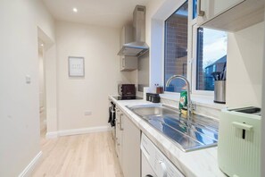 A modern kitchen with a built-in dishwasher, a stainless steel sink, and a window overlooking a brick exterior. - Modern 2BR Home • Private Driveway • Near Airport (Wythenshawe)