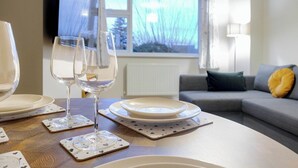 Una mesa de comedor con platos, vasos y posavasos, ubicada en un cuarto con un sofá y una ventana que da a vista de árboles.
