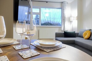A dining table with plates, glasses, and coasters, set in a room with a sofa and a window with a view of trees. - Modern 2BR Home • Private Driveway • Near Airport (Wythenshawe)