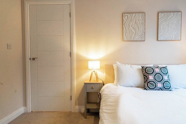 A bedroom with a bed, a nightstand with a lamp, and two wall-mounted artworks.