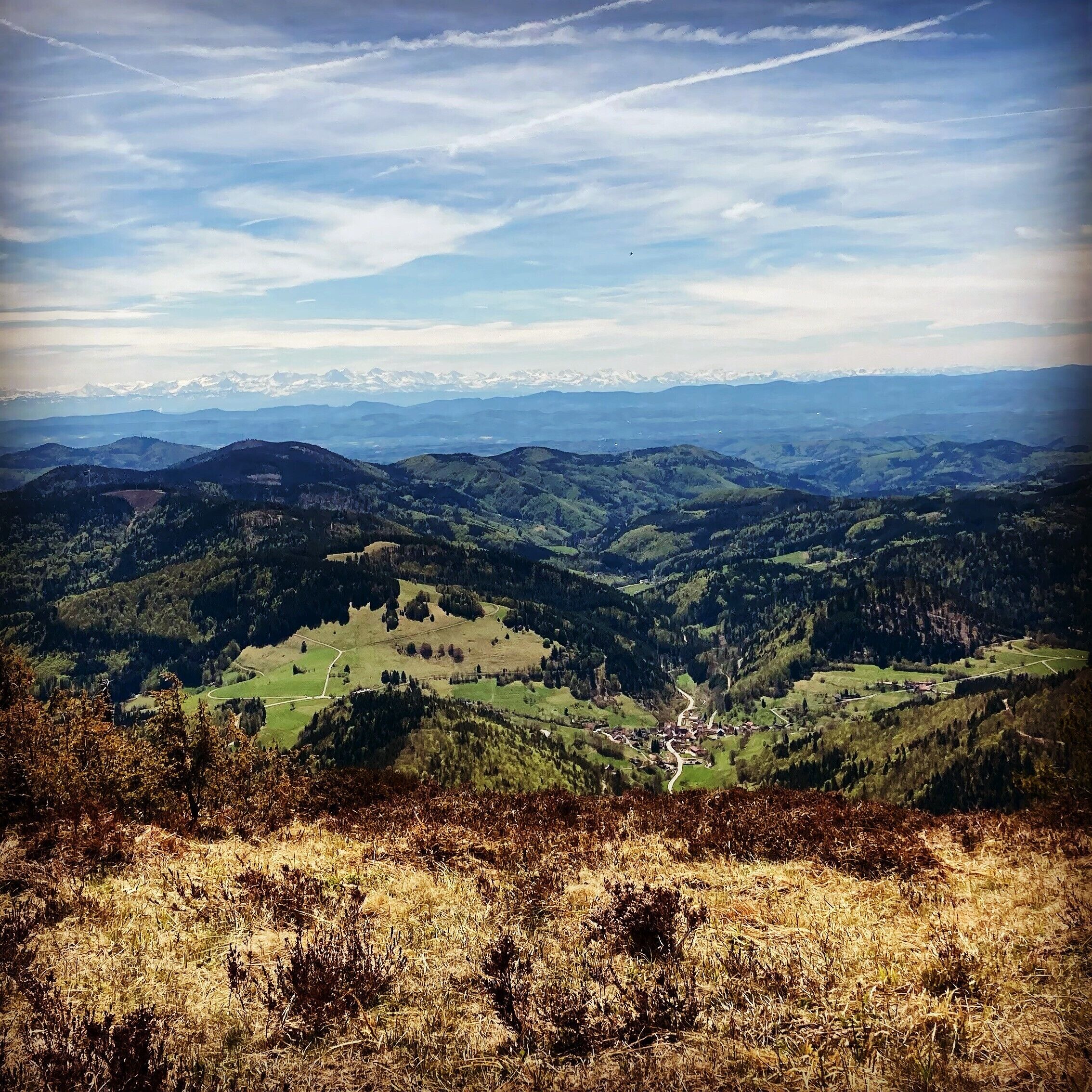 Una vista panoramica su una valle con un piccolo villaggio, circondato da montagne e un cielo sereno.