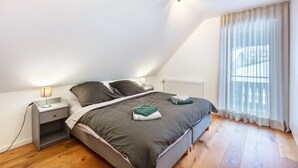 Ein Schlafzimmer mit Bett, Nachttisch, Lampe und einem Fenster mit Vorhängen.