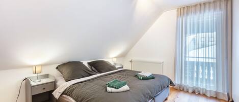 Une chambre à coucher avec un lit, une table de chevet, une lampe et une fenêtre avec des rideaux.