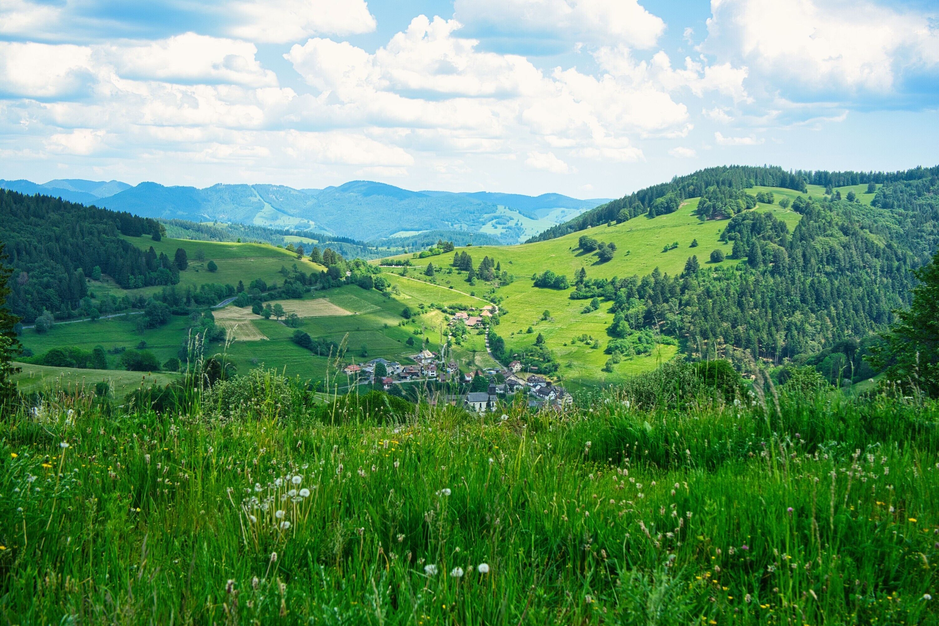 A rural landscape with rolling hills, a small village, and a clear sky.