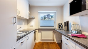 Eine moderne Küche mit weißen Schränken, einem Backofen, einem Fenster mit Blick auf ein Haus und einer Mikrowelle.