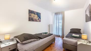 Ein Schlafzimmer mit zwei Betten, einem Nachttisch mit Lampe, einem Bild an der Wand und einem Fenster mit Vorhängen.