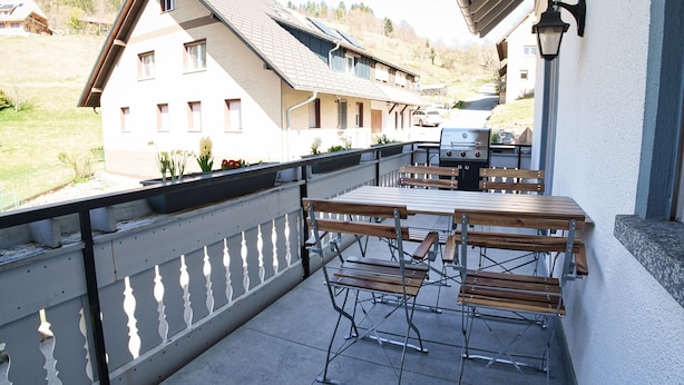 Ein Balkon mit Sitzgelegenheit, Blick auf ein Haus und ein geparktes Fahrzeug.