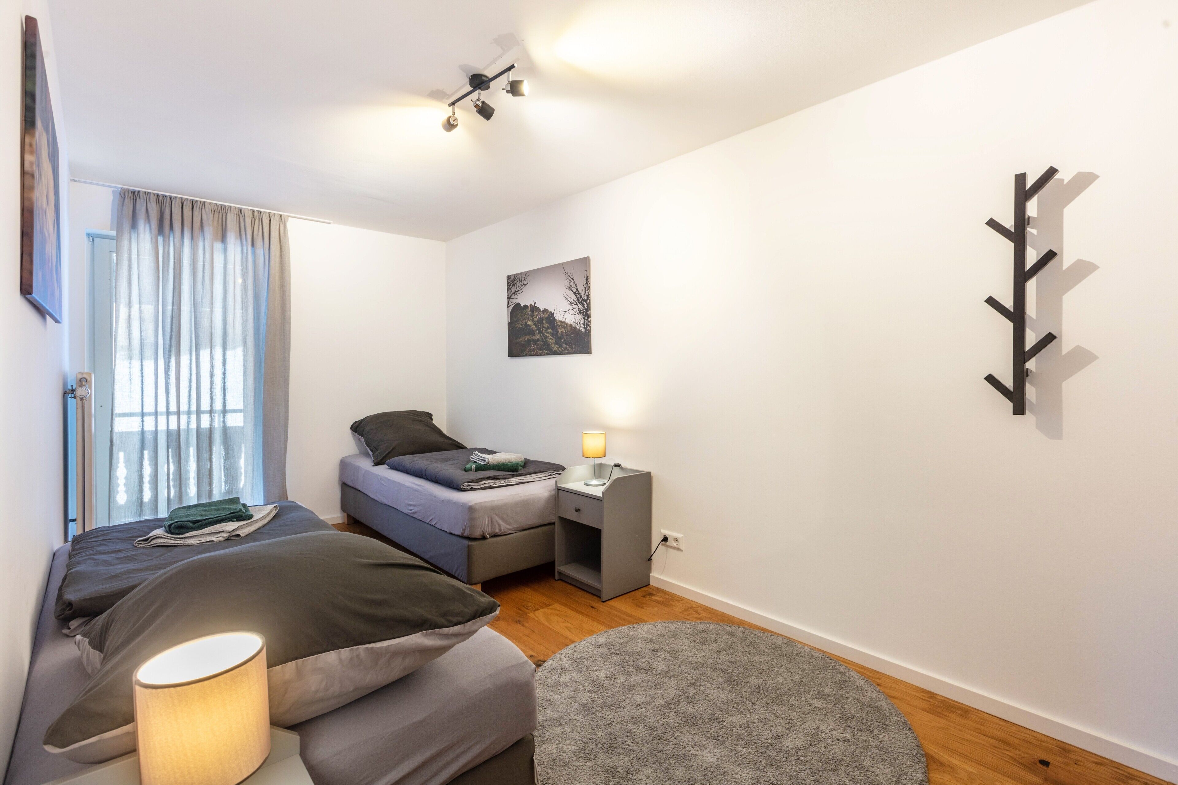 A bedroom with two beds, a bedside table with a lamp, a wall-mounted coat rack, and a picture on the wall.