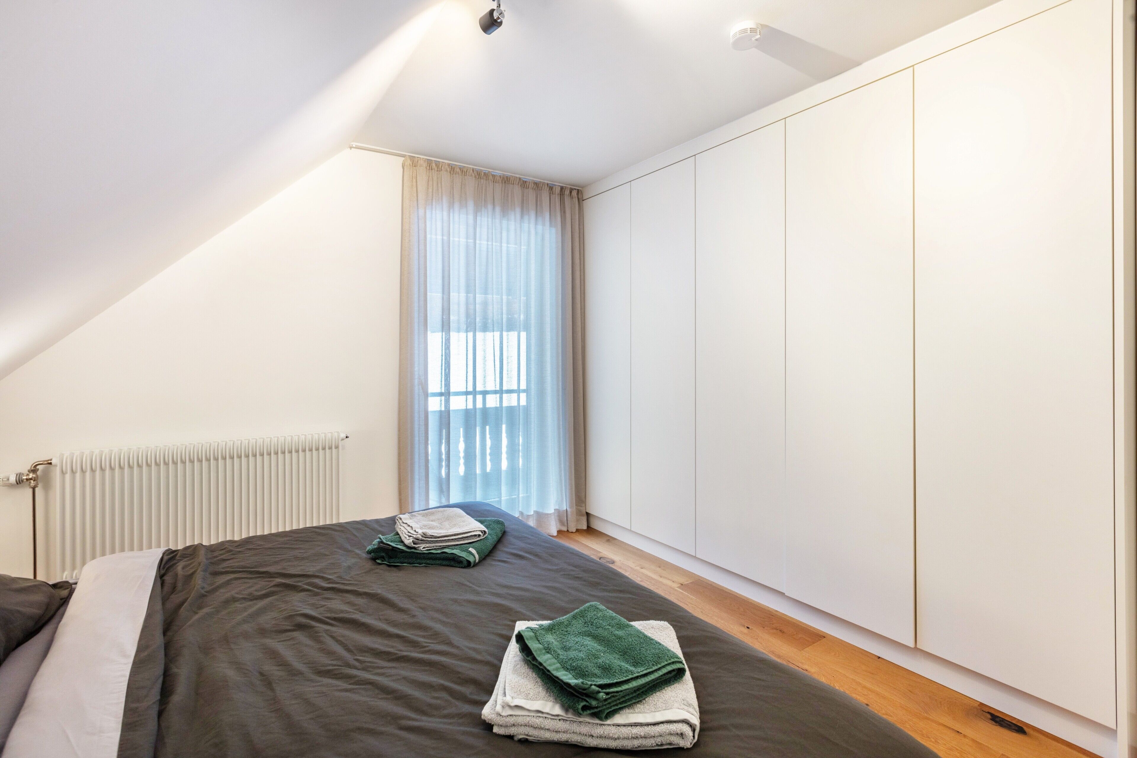 Un dormitorio con cama, radiador, ventana con cortinas y armario.