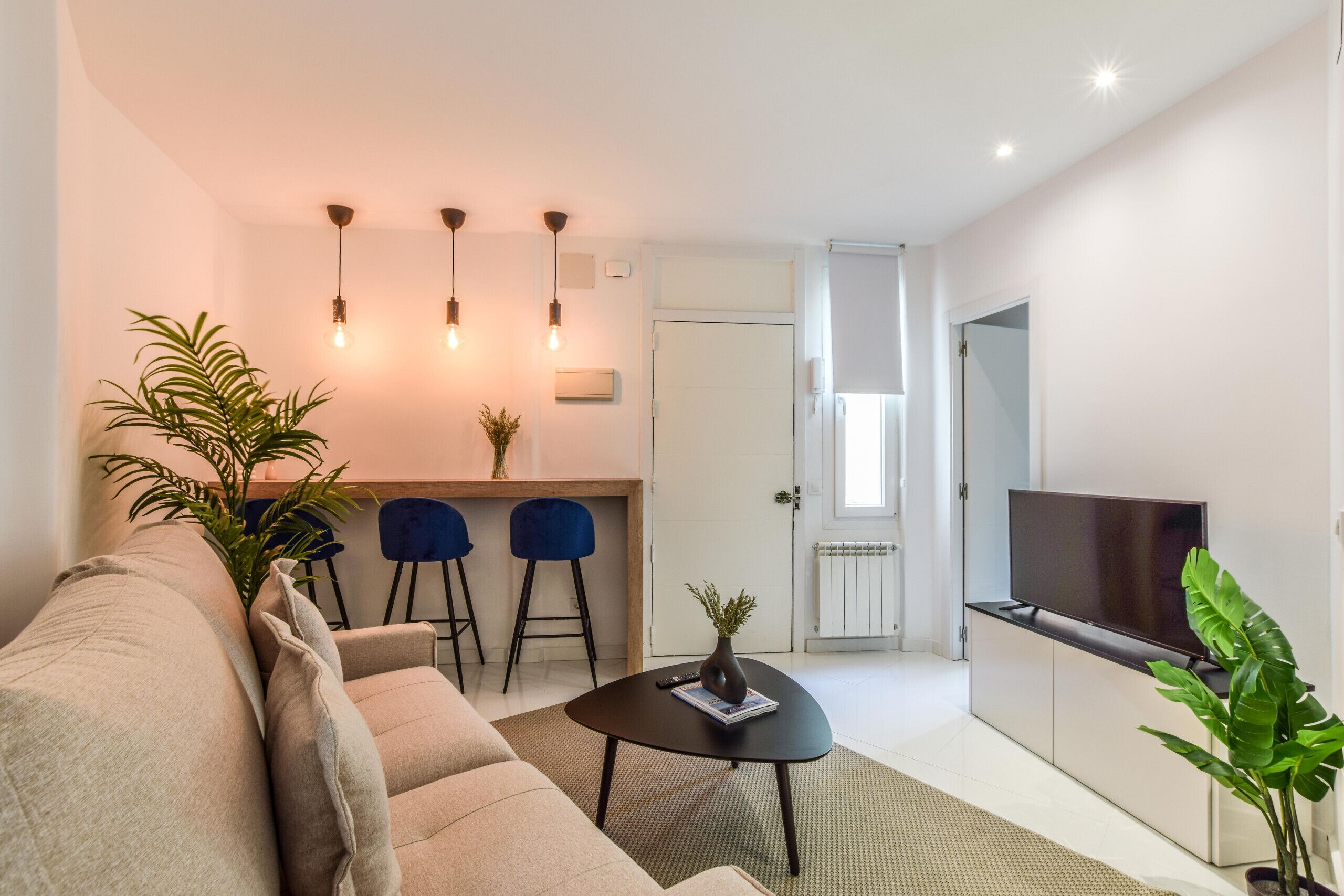A modern living room with a sofa, a coffee table, a TV, and a dining area with chairs and a small table.