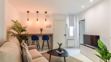 A modern living room with a sofa, a coffee table, a TV, and a dining area with chairs and a small table.