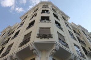 Un immeuble à plusieurs étages de style architectural classique, doté de balcons avec des garde-corps en fer forgé et d’une entrée centrale ornée d’une colonne décorative.