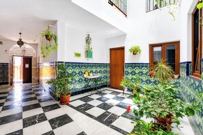 A hotel lobby with a checkered floor, potted plants, a tiled wall with a geometric pattern, and a wooden door.