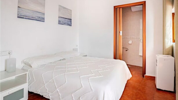 Ein Schlafzimmer mit einem Bett, einem Nachttisch, einer Wandsteckdose und einer Tür zu einem Badezimmer.
