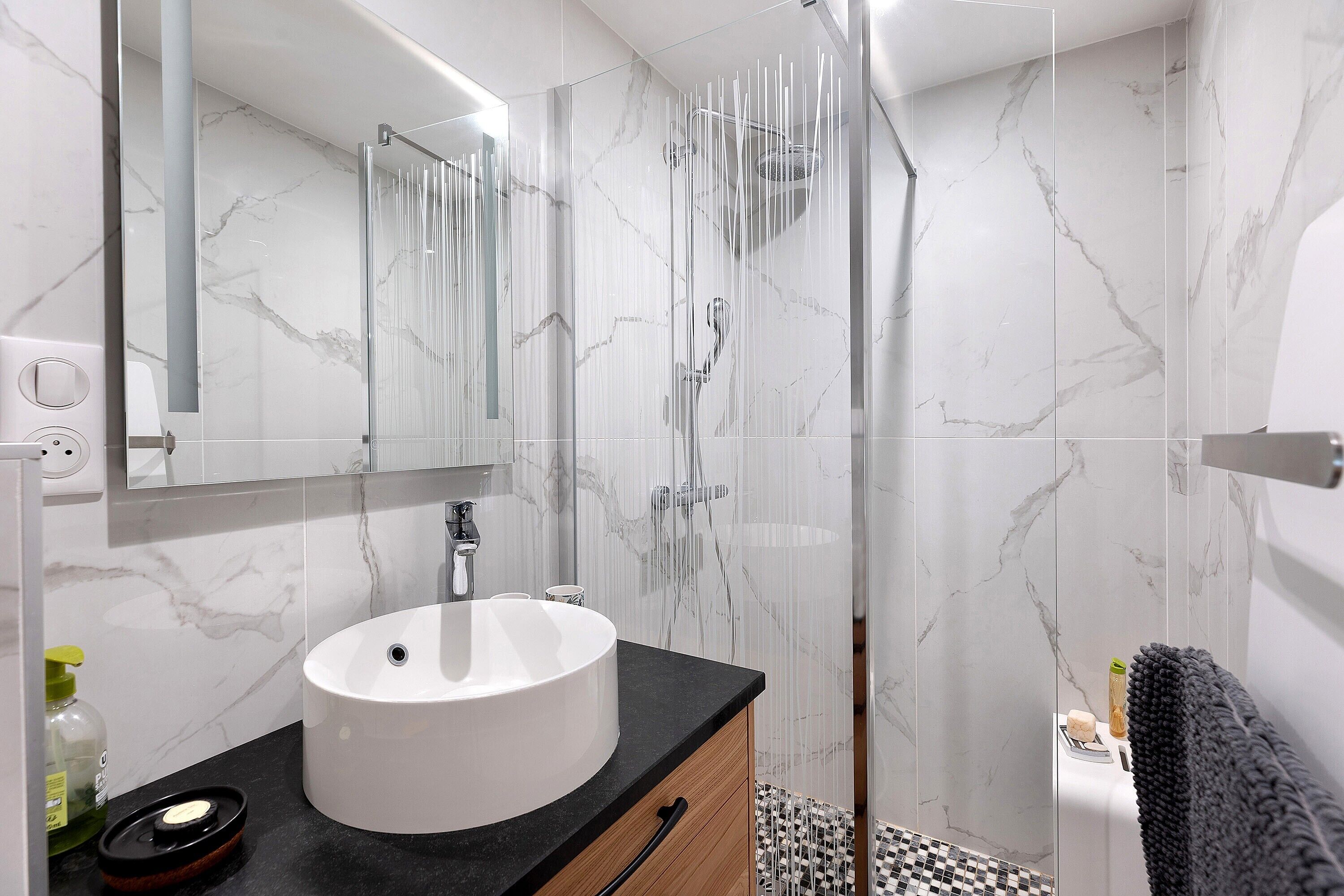 A modern bathroom with a marble wall, a round sink, a glass shower enclosure, and a black towel.