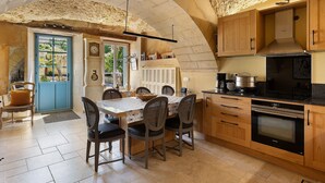 Een keuken met een stenen plafond, houten kasten, een ingebouwde oven en een eettafel met stoelen.