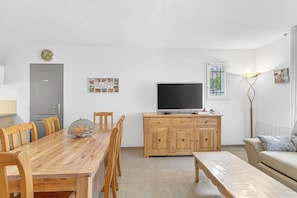 Un comedor con una mesa y sillas de madera, un televisor sobre un mueble de madera, un banco y un sofá.