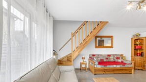 A living room with a sofa, a wooden coffee table, a wooden staircase, a small table with a lamp, and a wooden cabinet.