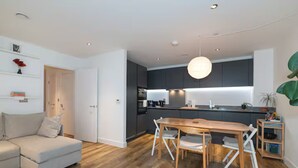 Een moderne keuken met donkere kastjes, een houten eettafel en inbouwverlichting.