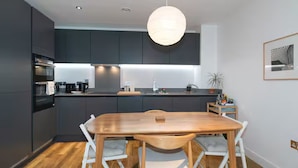 Een moderne keuken met donkere kastjes, een houten eettafel en een hanglamp.