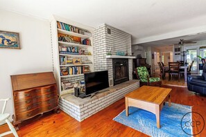 A living room with a fireplace, bookshelves, a television, and a dining area. - White Pines Cottage on Lake Michigan (Montague)