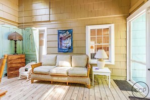 A cozy room with a wicker sofa, a small white table, a lamp, and a poster on the wall. - White Pines Cottage on Lake Michigan (Montague)