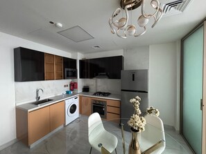 A modern kitchen with a dishwasher, stove, and refrigerator. There is a dining area with a glass table and chairs. - Modern & Cozy 1BR in Al Furjan, Dubai fully furnished (Dubai)