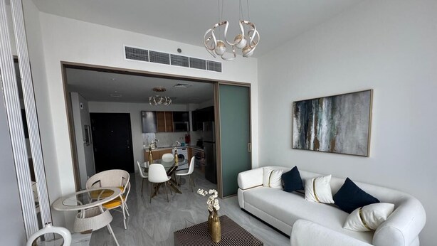 Ein modernes Wohnzimmer mit einem weißen Sofa, einem Esstisch und Stühlen. Durch eine offene Tür ist eine Küche zu sehen.