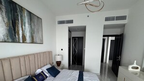 Ein modernes Hotelzimmer mit einem großen Bett, einem Nachttisch mit Lampe, einer Kommode und einem großen, abstrakten Gemälde an der Wand.