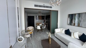 Ein modernes Wohnzimmer mit einem weißen Sofa, einem Esstisch mit Stühlen und einer Küche im Hintergrund.