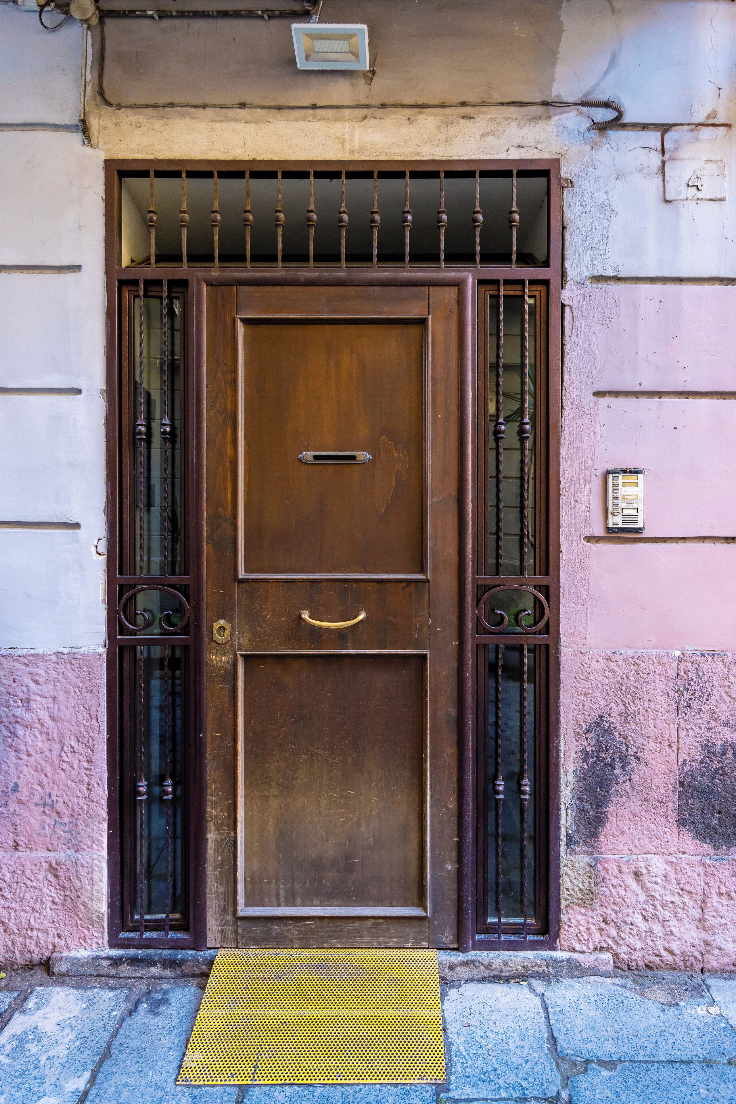 A brown wooden door with a metal gate and a yellow mat in front.