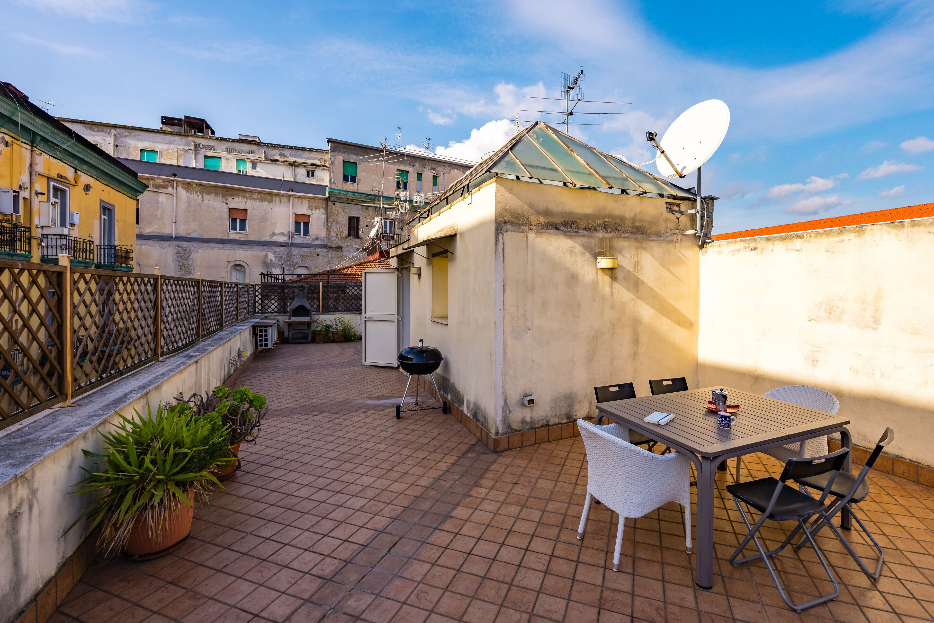 Eine Dachterrasse mit Tisch und Stühlen, Blumentöpfen, einem Grill und einer Satellitenschüssel.