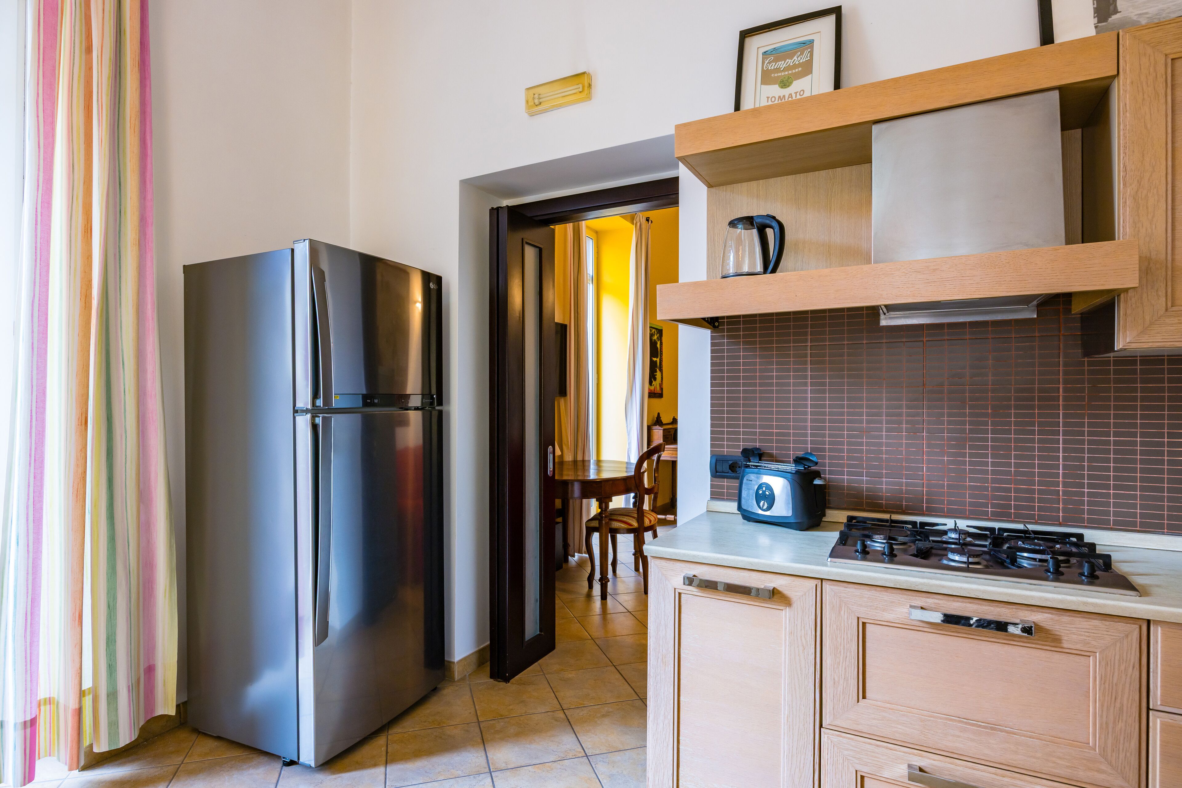 A kitchen with a stainless steel refrigerator, a gas stove, wooden cabinets, and a tiled backsplash.