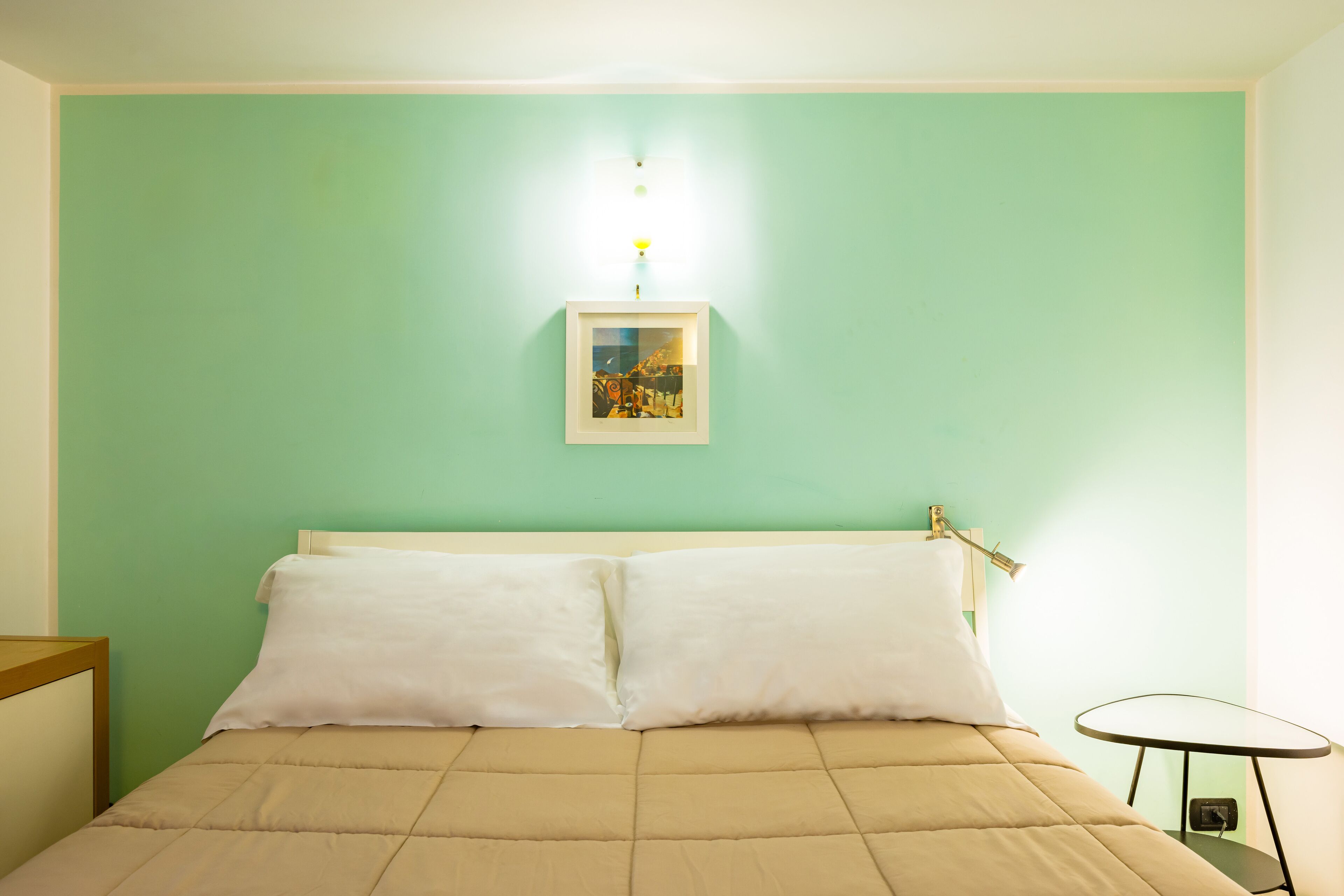 A bed with white bedding, a small bedside table, and a wall-mounted picture frame.