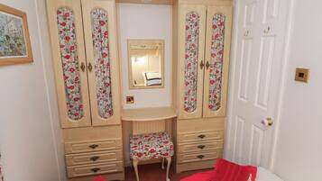 A bedroom with a bed, a small stool, a wooden wardrobe with floral panels, and a mirror above a dresser.