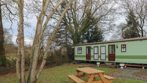 A green mobile home with a picnic table in a grassy area. - Rose Villa Caravan (Llandysul)